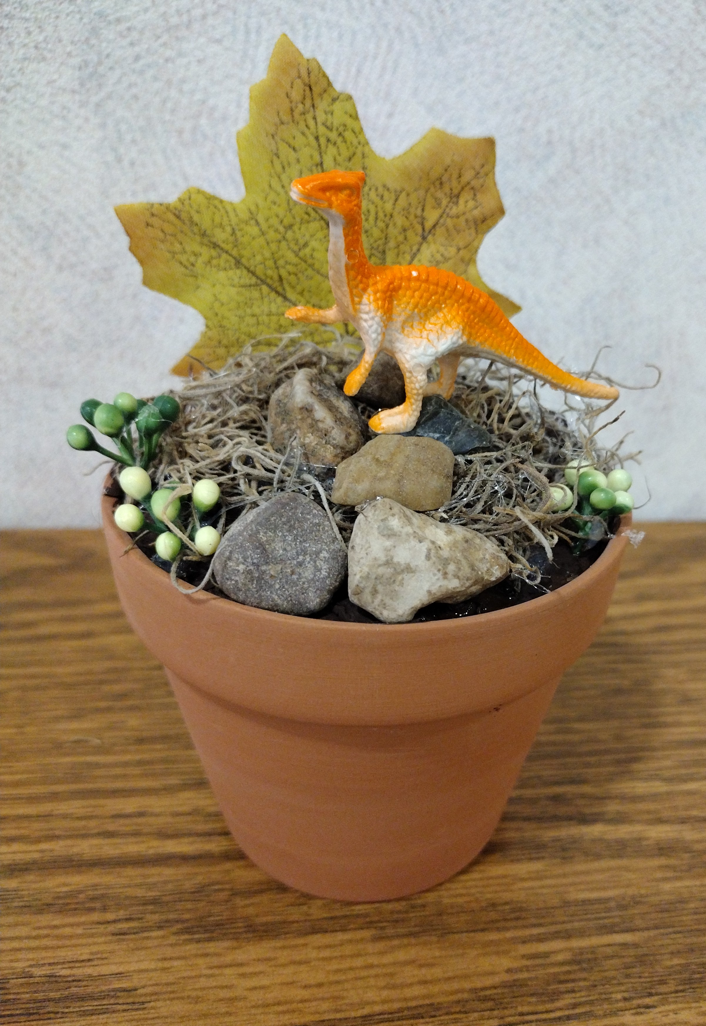 A flower pot with a small dinosaur habitat inside of it