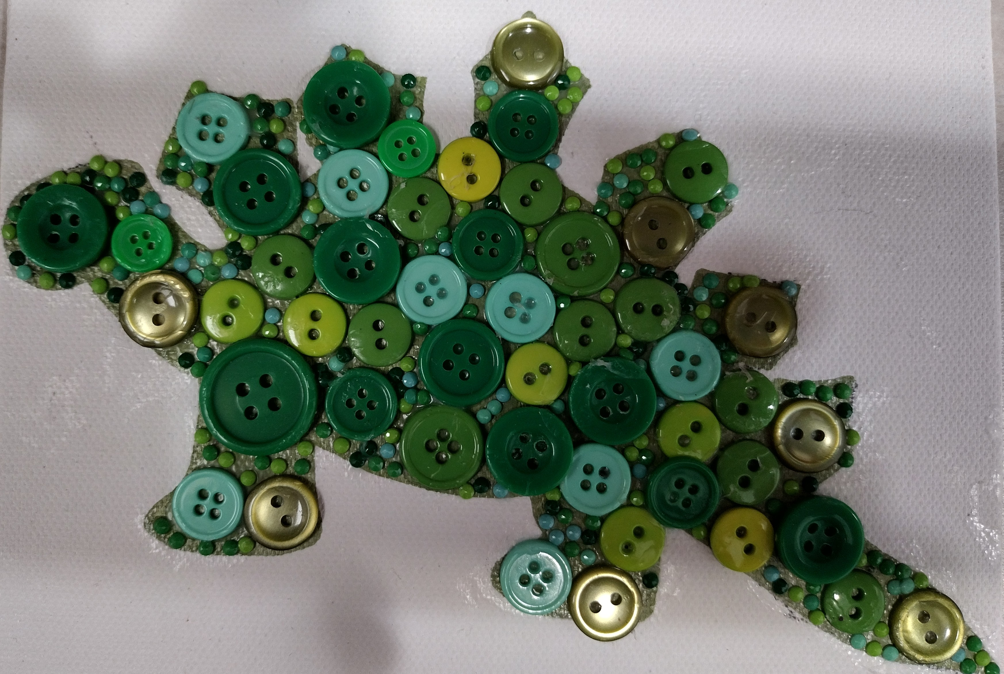 A dinosaur silhouette colored green and covered with green buttons. 