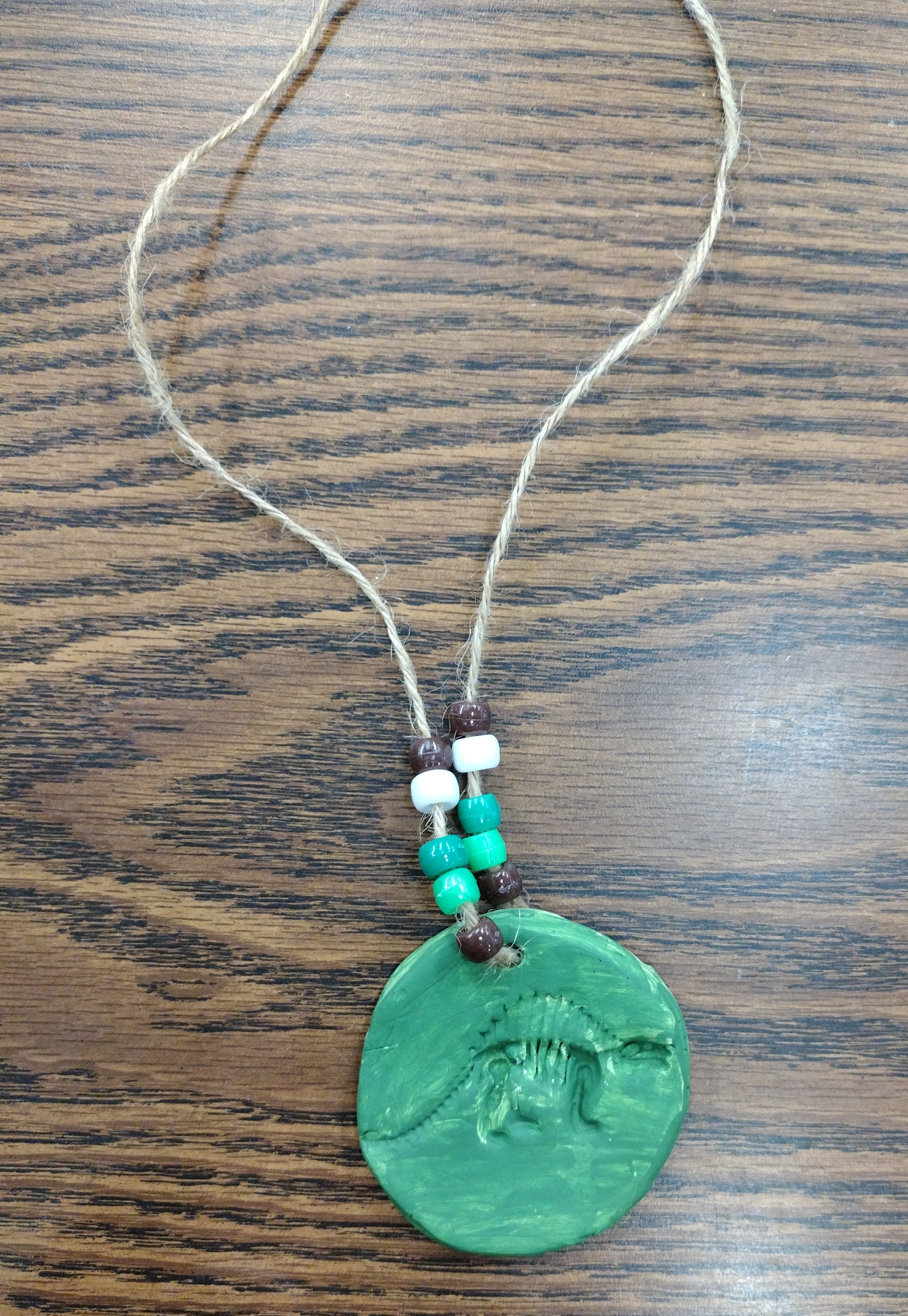An air dry clay circle with a dinosaur fossil imprint in it and made into a necklace with pony beads.