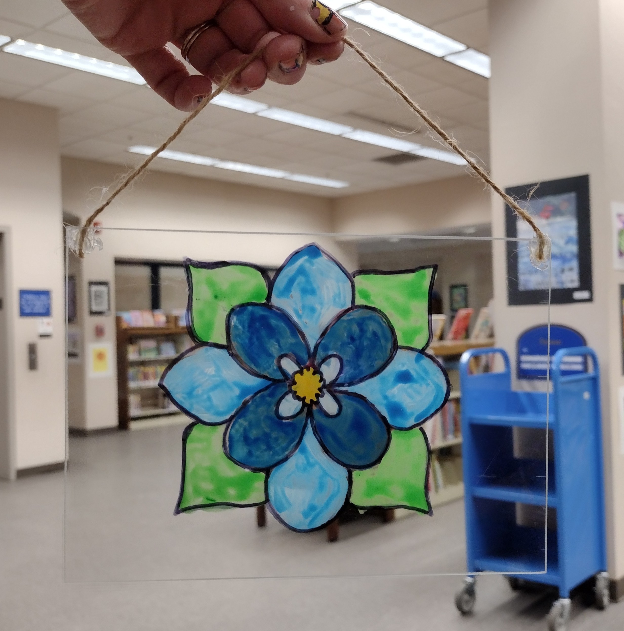 A blue and green flower painted on glass with jute string tied from the top