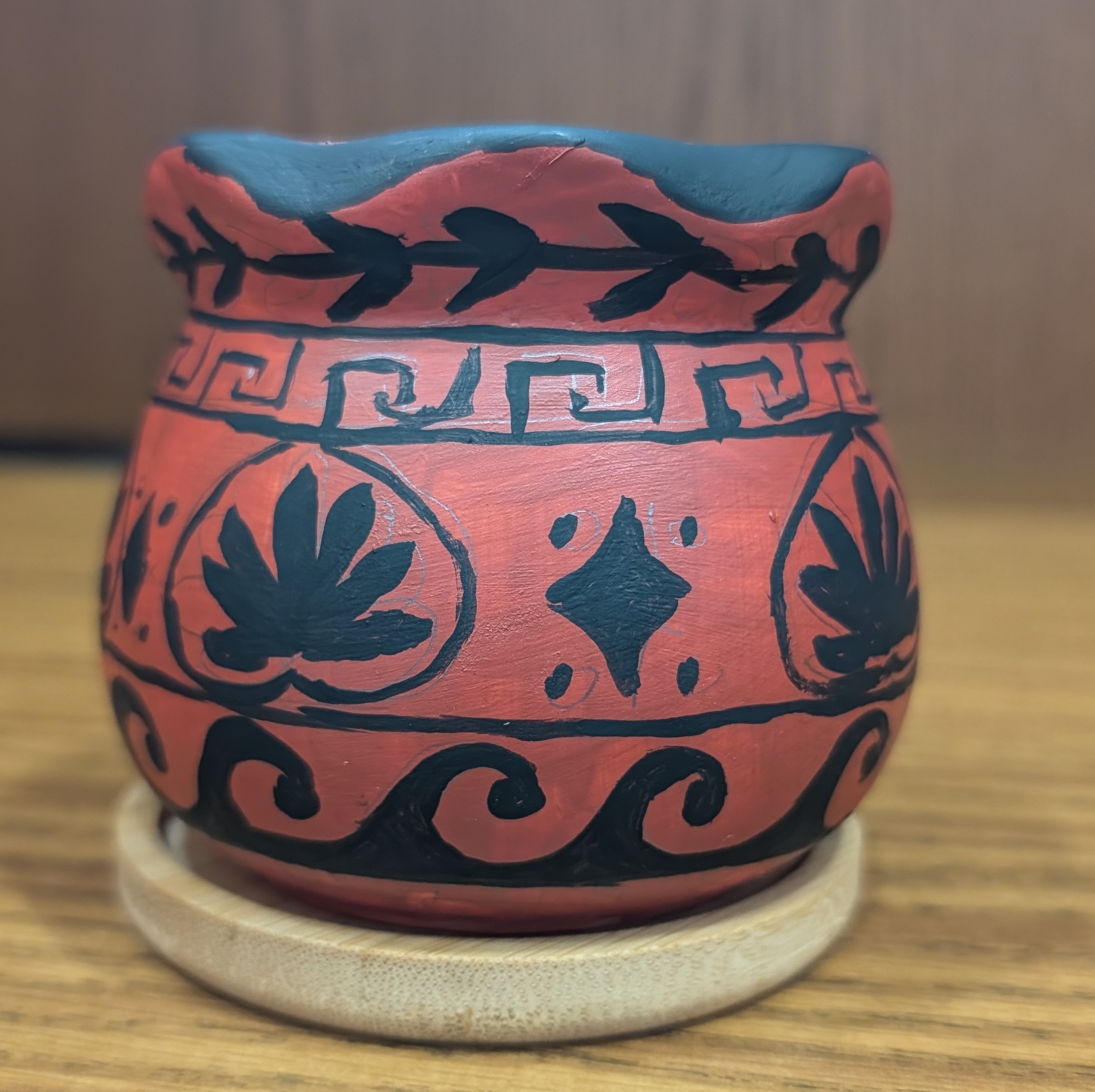 A small 3 inch pot painted reddish brown with patterns of Greek motifs painted in black 